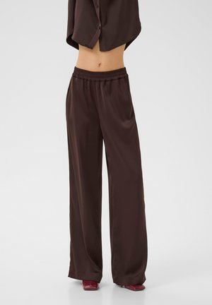 Brown satin wide-leg pants with an elastic waistband and smooth texture, paired with maroon heeled shoes.
