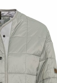 Helle graue gesteppte Jacke mit rundem Ausschnitt, Druckknopfverschluss und strukturiertem Stoff. Enthält ein Logopatch am Ärmel.