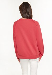 Rode sweatshirt met een gladde textuur, raglanmouwen en een losse pasvorm. Voorzien van een geribde onderrand en manchetten, gestyled met witte broeken.