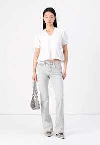 Fehér peplum top rövid puff ujjakkal, világosszürke harangnadrággal párosítva. A modell egy kis szürke táskával a kezében és fényes cipőben van.