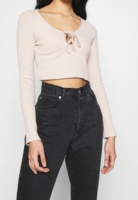 Top court à manches longues côtelé de couleur rose clair avec un détail en forme de trou de serrure noué au niveau du col, associé à un jean en denim noir taille haute.