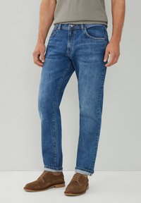 Jeans de denim azul claro con corte recto, que presentan un diseño clásico de cinco bolsillos y dobladillos enrollados, combinados con zapatos de ante marrón.