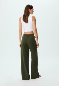 Top corto bianco senza maniche abbinato a pantaloni larghi in verde oliva a vita alta. Tessuto liscio, vita elastica e dettagli di design minimali.