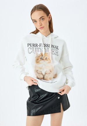 Hvid hoodie med et kattegrafik og teksten "PURR-FESSIONAL CUDDLER." Kombineret med en sort faux læderskirt.