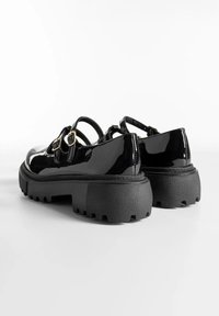 Chaussures en cuir verni noir avec une semelle chunky et texturée. Elles présentent deux brides avec des boucles dorées et un design à bout rond.