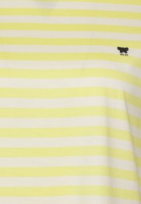 Stribet t-shirt med skiftende lysegule og hvide striber, lavet af blødt stof, med et lille sort broderet logo på venstre side.