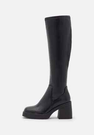 Botte en cuir noire montant au genou avec talon bloc épais et bout rond, montrée de profil sur un fond neutre.