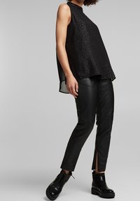 Sort ærmeløs top med høj halsudskæring og tekstureret stof, kombineret med sorte læderbukser med sideslidser og chunky sorte støvler.