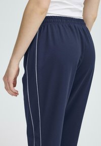 Námornícke joggers s elastickým pásom, so sivým bočným pruhom. Tkanina je hladká, s voľným strihom a uvoľneným dizajnom.