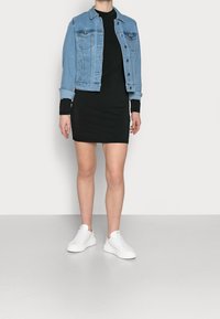 Vaaleansininen farkkutakki mustan mekon päällä, yhdistettynä valkoisiin tennareihin. Takissa on napit ja etutaskut.