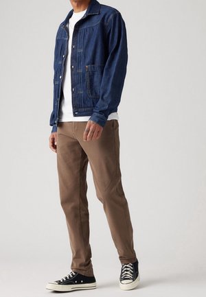 Džínová bunda v tmavě modré barvě s knoflíkovým zapínáním, doplněná světle hnědými chino kalhotami a černými teniskami. Vyznačuje se klasickým designem a náprsními kapsami.