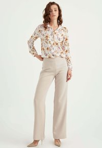 Bloemige blouse met lange mouwen in wit, crème, oranje en paarse tinten; gecombineerd met beige wijde broek en nude puntenhakken.