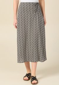 Falda midi de estampado floral en azul marino y crema, hecha de una tela ligera. Presenta una cintura con lazo y una silueta fluida, combinada con sandalias negras de tiras.