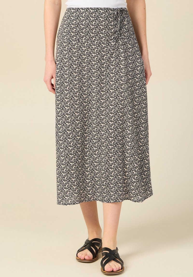 Falda midi de estampado floral en azul marino y crema, hecha de una tela ligera. Presenta una cintura con lazo y una silueta fluida, combinada con sandalias negras de tiras.