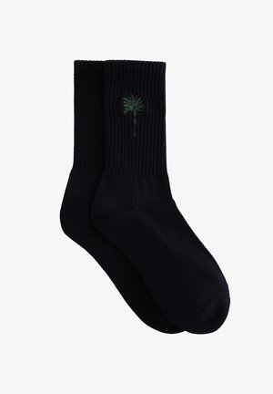 Calzini neri a coste con piccolo ricamo verde a forma di palma sul lato esterno di ogni calzino.