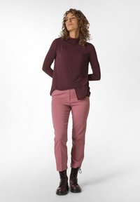 Burgundy langærmet top med svalehals, parret med lyserøde slim-fit bukser og mørke snørebåndsstøvler. Glat tekstur gennem hele outfittet.