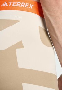 Beige elastic leggings with a large tan graphic pattern, featuring an orange waistband labeled "TERREX" and "CLIMACOOL" tag detail.