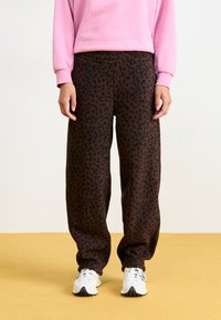 Braune Leopardenmuster-Sweatpants mit lockerer Passform, elastischem Bund und weichem Material, kombiniert mit weißen Sportschuhen.