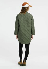 Olivovo zelený prešívaný dlhý kabát s okrúhlym lemom a dlhými rukávmi. Skombinovaný s čiernymi legínami a hnedými členkovými čižmami.