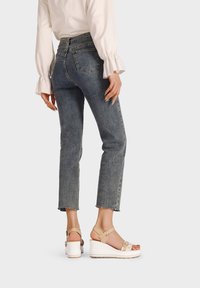 Jeans in denim scuro a vita alta con orlo sfrangiato abbinati a sandali platform beige chiaro con cinturini alla caviglia e dettagli testurizzati.