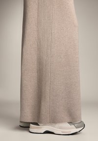 Beige stickad klänning med vertikal ribbad textur längs sidan, tillsammans med ljusgrå och vita träningsskor. Slät tygfinish.