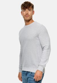 Pull en maille grise avec un motif texturé, encolure ronde et poignets côtelés, associé à un jeans bleu.