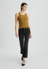 Débardeur côtelé moutarde, jeans noirs évasés et chaussures plates noires. La tenue présente un design ajusté avec des accents matériels simples.