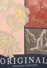 Λουλουδένια σχέδια σε κίτρινα, κόκκινα και μπεζ τετράγωνα με τα κείμενα «ORIGINAL» και «DESIGNED IN COPENHAGEN» σε σκουρό μπλε υφασμάτινο φόντο.