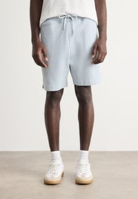 Light blue ribbed shorts with elastic waistband and drawstring. Features side vents and logo accent. Worn with white sneakers and socks.