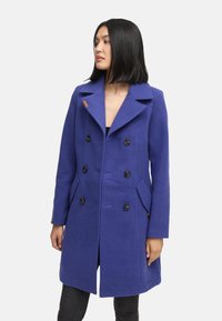 Purple wool peacoat featuring a double-breasted design, large black buttons, and side pockets. Notable wide collar and sleek fit.