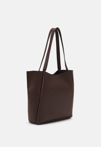 Brązowa torba na ramię wykonana z gładkiego materiału. Posiada dwa długie paski, otwartą górę oraz minimalistyczny design z dyskretną zewnętrzną kieszenią.