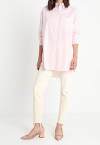 Camicia a maniche lunghe a righe rosa chiaro con taschino, abbinata a jeans bianchi a vita alta e scarpe con tacco a blocco perforate in rosa.