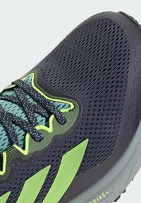 Sneaker in rete blu scuro con accenti verde lime, caratterizzata da una superficie testurizzata, strisce con logo prominenti e occhielli rinforzati per i lacci.