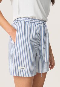 Shorts légers rayés bleu et blanc avec une taille élastique, des poches latérales et un détail à nouer, comportant une petite étiquette "trempée".
