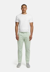 White cotton t-shirt, light green cotton pants. Model stands upright, wearing grey sneakers. Plain design, no visible patterns or logos.