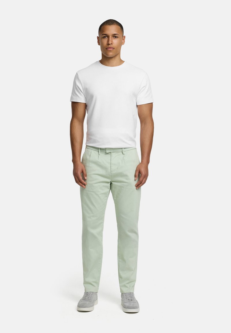 White cotton t-shirt, light green cotton pants. Model stands upright, wearing grey sneakers. Plain design, no visible patterns or logos.