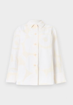 Camisa branca com padrão floral em amarelo suave, gola pontiaguda, mangas compridas e seis botões à frente. Confeccionada em tecido leve.