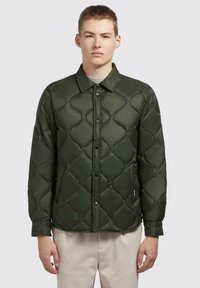Gevulde groene jack met een gequiltte textuur, met drukknopen aan de voorkant en een kraag. Draagt over een lichtgekleurde shirt.