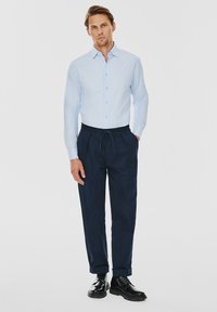 Jasnoniebieska koszula na guziki, granatowe spodnie z troczkami, czarne buty. Koszula w wąski kroju, a spodnie mają strukturalne wykończenie.