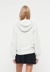 Felpa grigia chiaro con cappuccio e vestibilità rilassata, caratterizzata da spalle scese e polsini a costine, abbinata a una gonna plissettata nera.