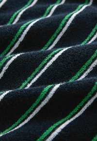 Gros plan sur un tissu sombre texturé avec des rayures diagonales vertes et blanches créant un motif ondulé.