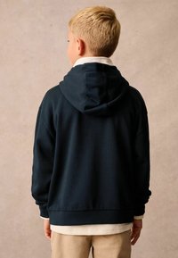 Sudadera azul marino con una gran capucha, puños y dobladillo acanalados, confeccionada con una tela suave, superpuesta a una camiseta de color claro, vista desde la parte posterior.