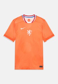 Oransje Nike-drakt med et løveemblemat, prikkete mønster, kontrasterende rød og blå krage, korte ermer og teksturert stoff.