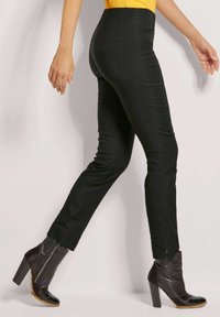 Schwarze, figurbetonte Hose mit glatter Textur und schlanker Silhouette, mit Schlitzen an den Knöcheln. Getragen mit schwarzen, geschnürten, knöchelhohen Stiefeln.