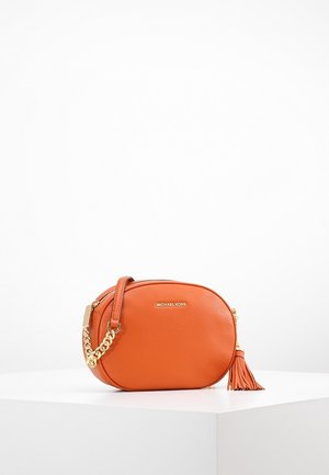 Orange læder oval crossbody taske med guldkæde rem, kvast detalje og Michael Kors logo på forsiden, placeret på en hvid piedestal.