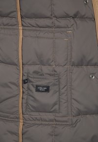 Intérieur d'une veste matelassée grise avec une poche cousue portant l'étiquette "CARELABEL INSIDE" et une étiquette de taille indiquant "38" près du bord de la poche.