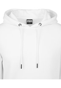 Sudadera blanca con capucha ajustable, ojetes de metal y una etiqueta impresa en el interior. Tejido suave con una textura lisa.