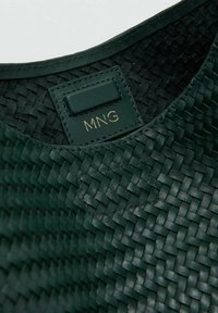 Sac en cuir tressé vert présentant une surface texturée, un léger éclat et une étiquette "MNG" en relief doré à l'intérieur.