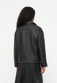 Μαύρο δερμάτινο μπουφάν με δομημένο γιακά, ορατές ραφές και κοντό σχέδιο, συνδυασμένο με ασπρόμαυρη φούστα.