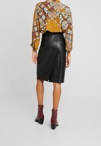 Černá kožená tužková sukně se zadním rozparkem, doplněná barevnou vzorovanou blůzou. Burgundské kotníkové boty outfit dokončují.